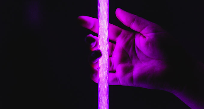 En hand spelar på en platssträng i ett lila ljussken